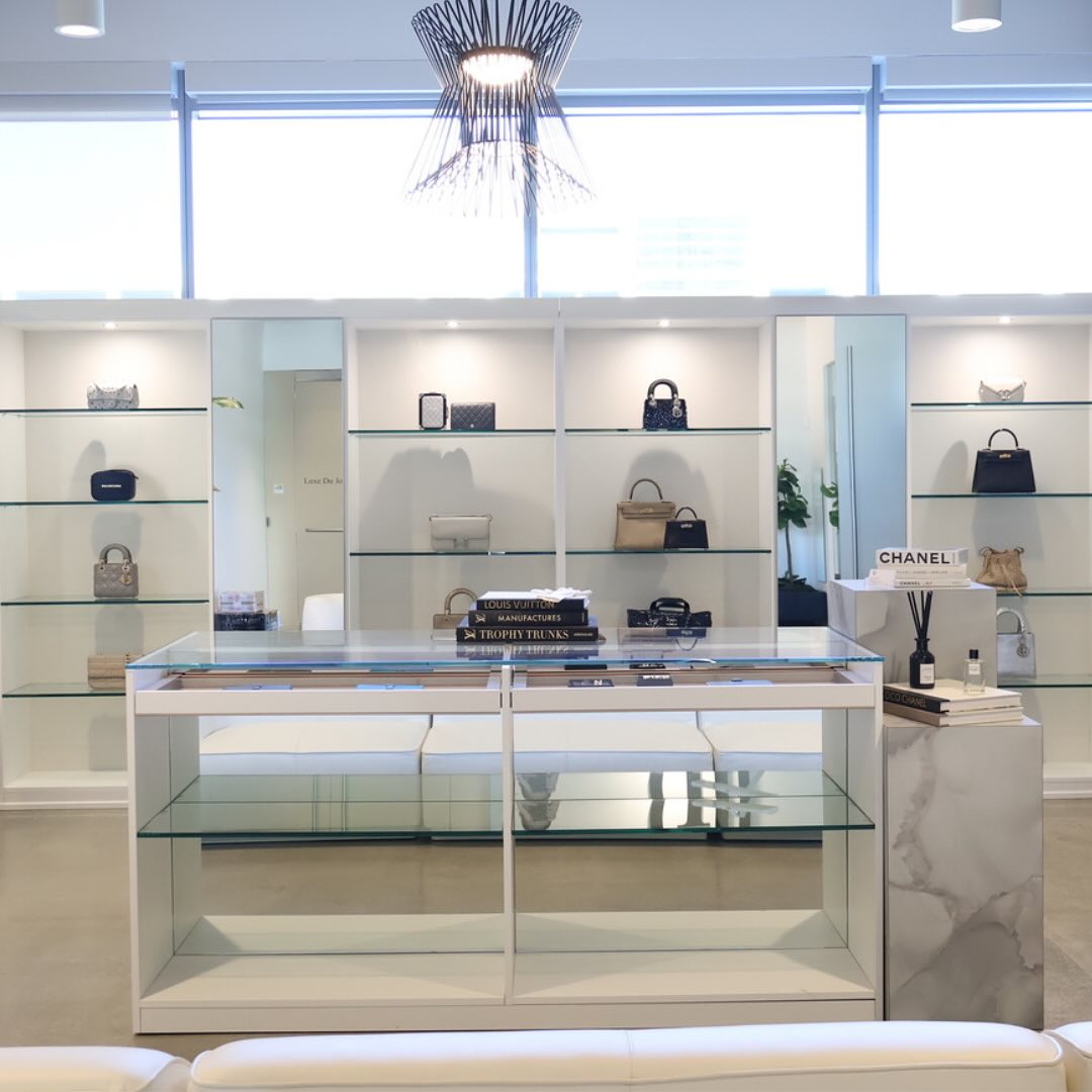 White glass and marble display cases with Chanel handbags on shelves in a bright boutique interior