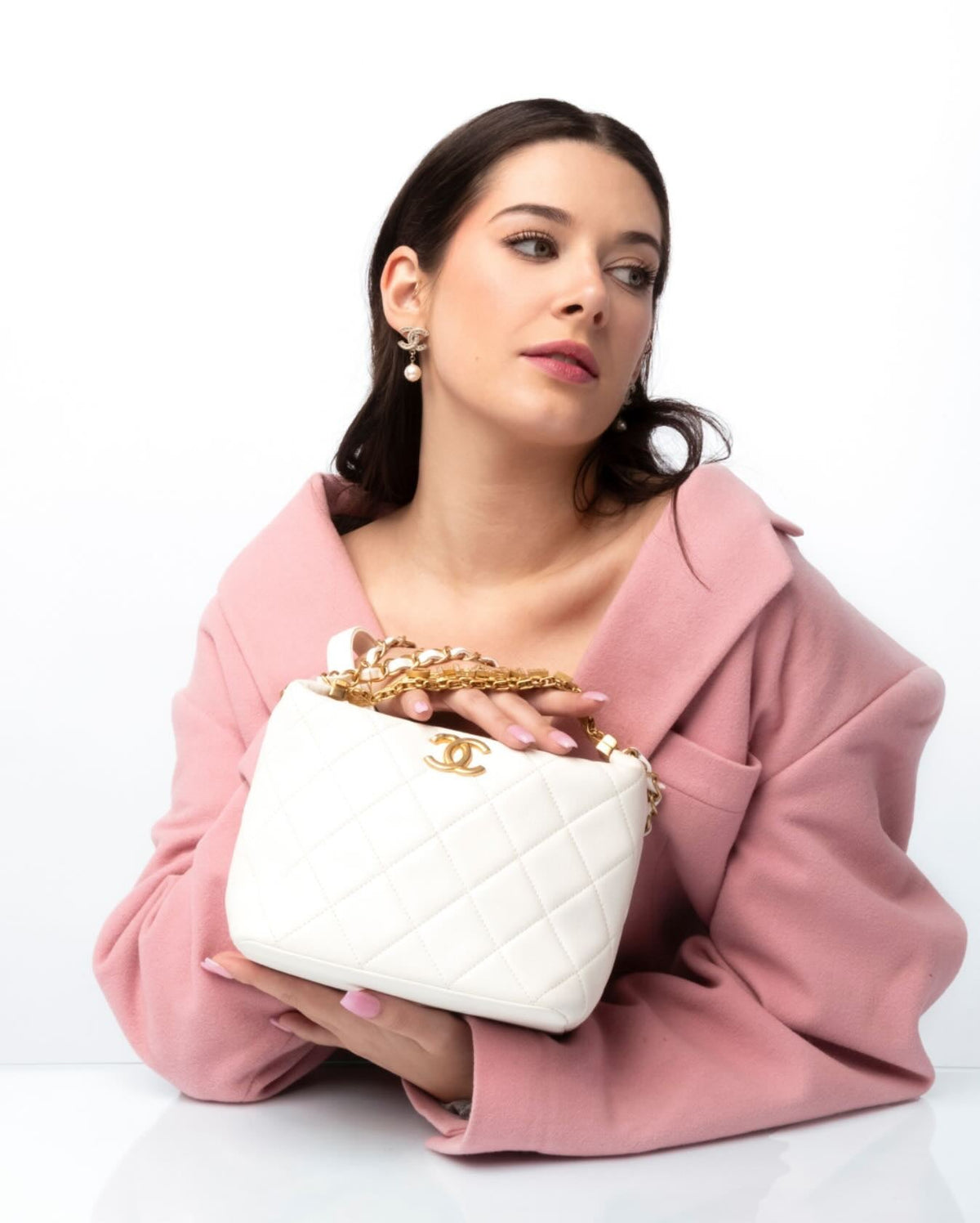 woman wearing pink coat holding white quilted leather Chanel handbag with gold chain hardware