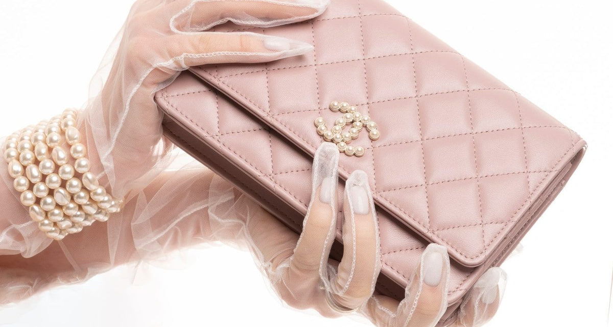 Chanel pink quilted leather wallet with gold hardware held by hands wearing sheer gloves and pearl bracelets