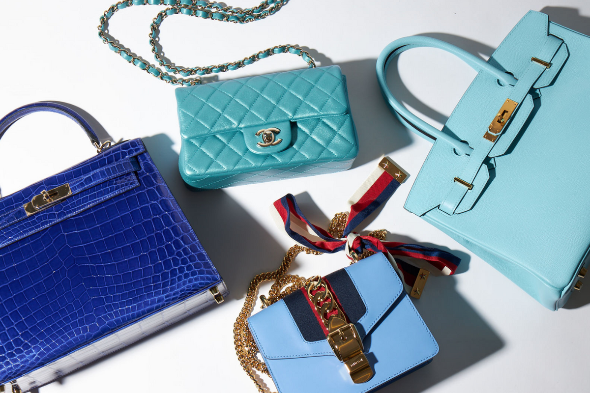 Four luxury handbags in shades of blue arranged on a white surface with varied textures and hardware details