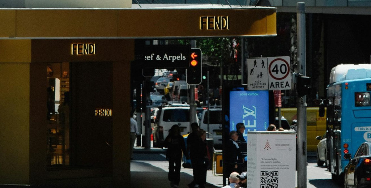 Fendi store entrance with gold signage on a city street with pedestrians and vehicles