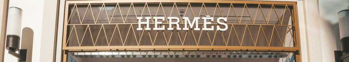 Hermès store entrance with a gold and glass sign displaying the Hermès logo above the door